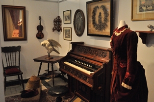Interior view of an exhibit featuring historic artefacts, including a piano and artwork.